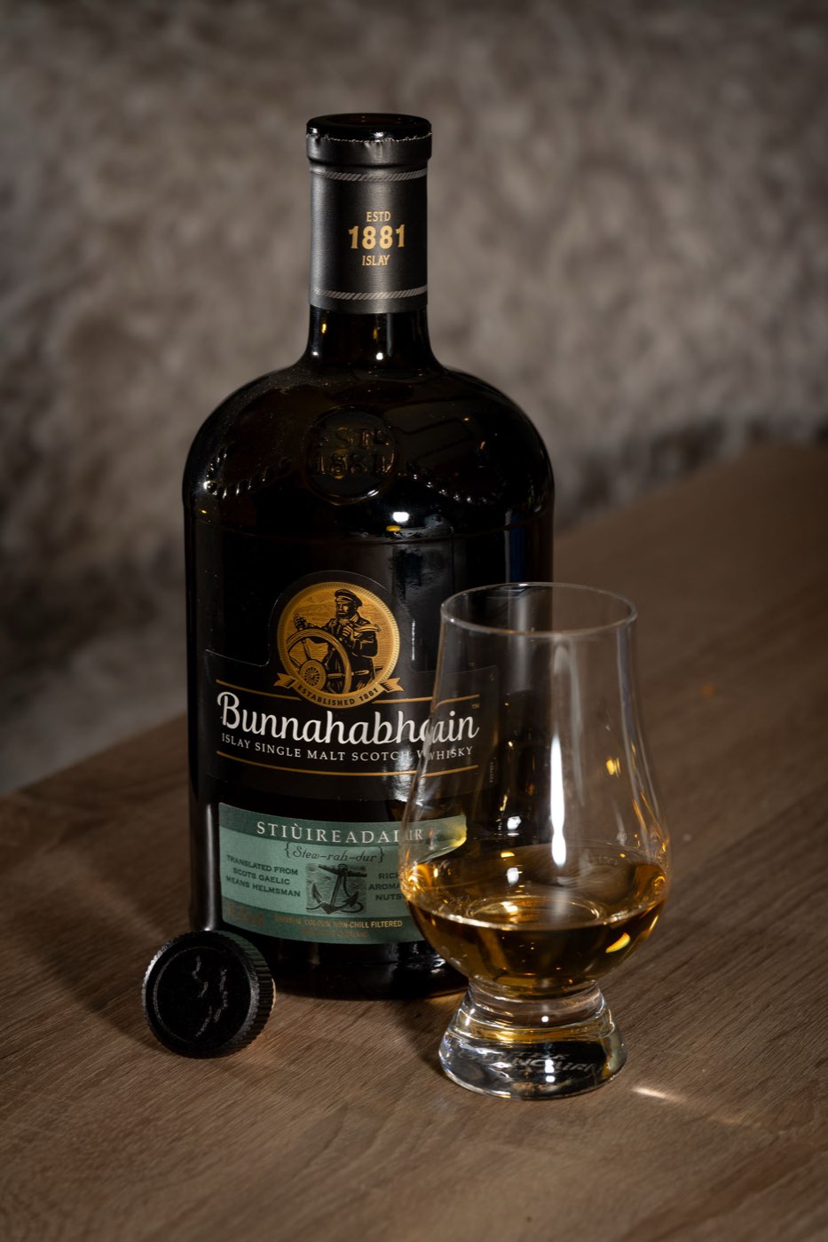 Bunnahabhain Stiùireadair bottle beside a filled Glencairn glass and cork on a wooden table