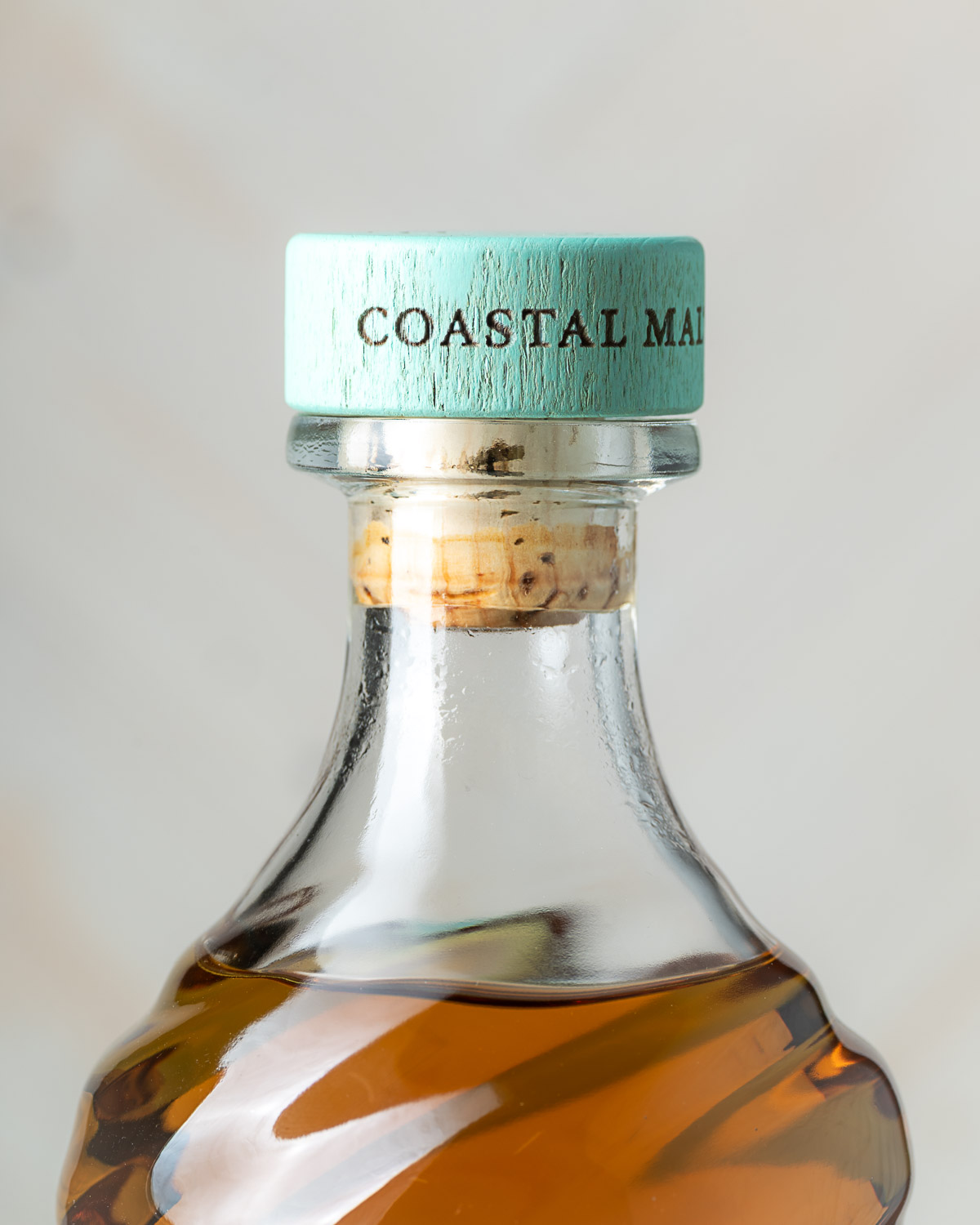 Close-up of the bottle neck and mint-green Coastal Malt cap with cork visible