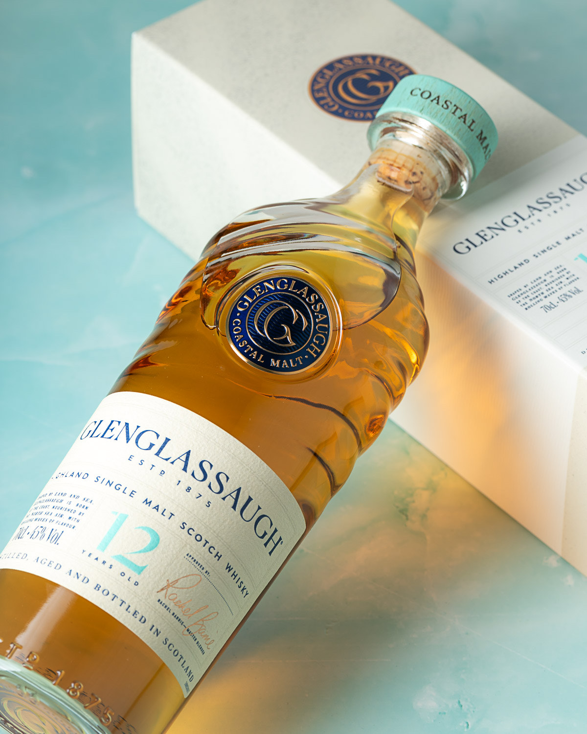 Angled view of the bottle beside its packaging box on a teal background
